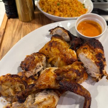 A platter of Portuguese chicken with a bowl of rice in the background.