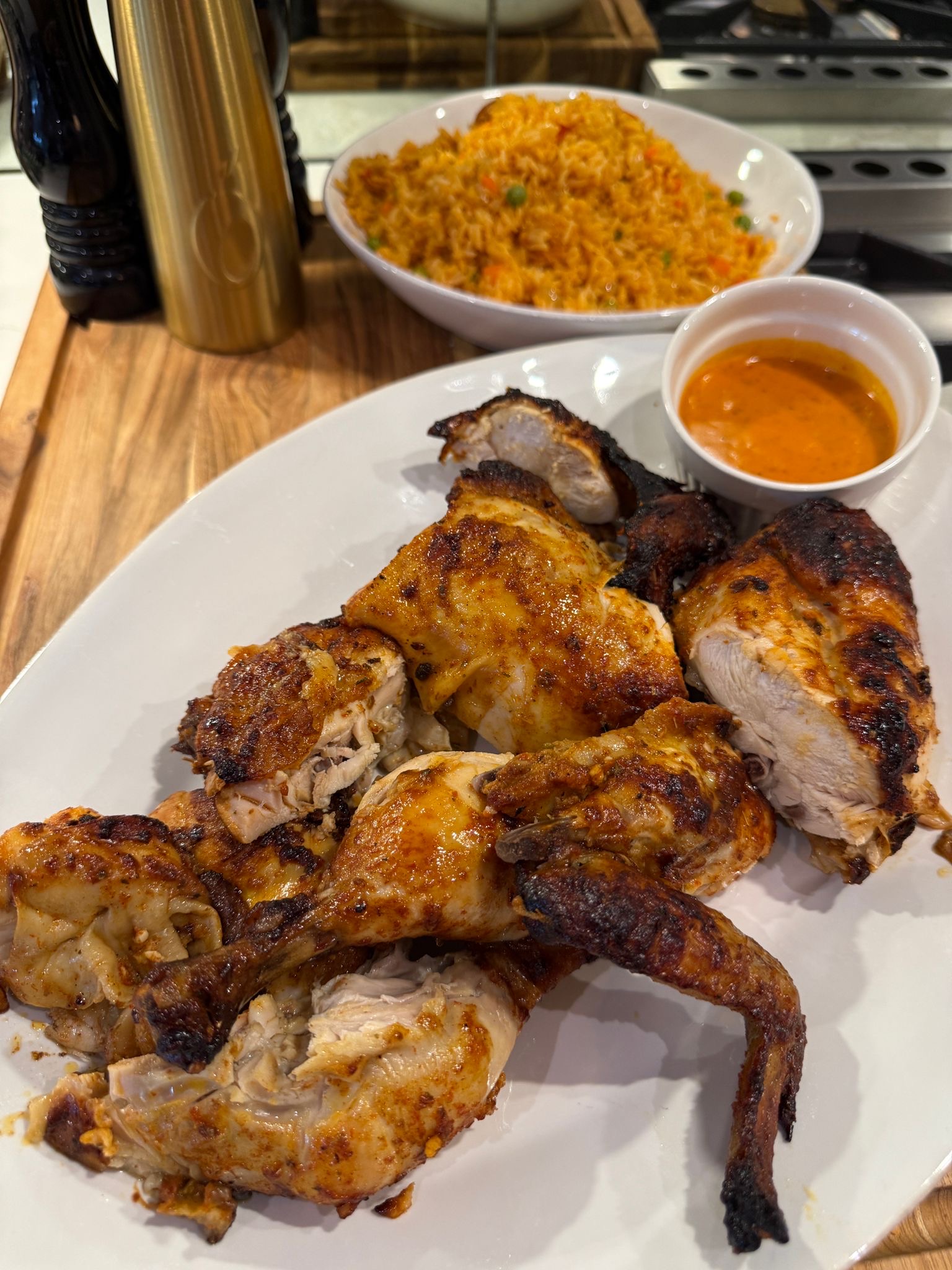 A platter of Portuguese chicken with a bowl of rice in the background. 