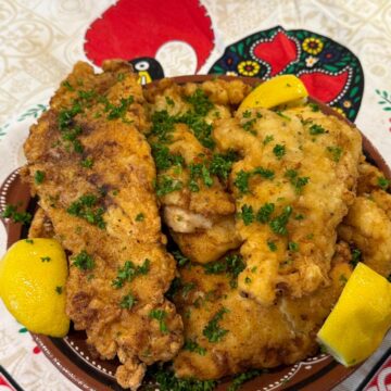 Filetes de Peixe on a plate with lemon wedges.